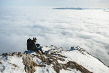 Adult male hiker sitting on rocky mountain above clouds 
