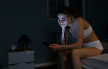 Woman With Sleep Disorder Using Cellphone In Bedroom