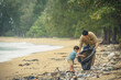 Asian father and son of volunteer people collecting trash on beach. Ecology charity and clean environment earth day concept.