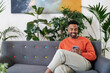 © Studio Marmellata/Stocksy - Cheerful man using smartphone on sofa in modern house