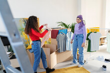 Woman Unpacking Box And Showing Clothes To Arab Friend