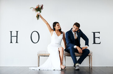 Wall Mural - Who wants the bouquet. Concept studio shot of a bride and groom making an V in the word love against a wall.