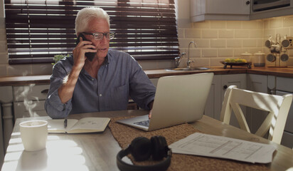 Sticker - Old age hasnt stopped me from working. Shot of a senior man sitting alone in the kitchen and using technology to work from home.