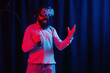 © endrews21 - a man with a long black beard in gray golf and virtual reality glasses with a bottle of soda in neon light on a dark background explores the metaverse