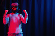 © endrews21 - an adult bearded man in a gray golf and virtual reality glasses in neon light on a dark background jumps and rejoices in victory
