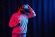© endrews21 - a man with a long black beard in gray golf and virtual reality glasses with a bottle of soda in neon light on a dark background explores the metaverse