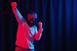 © endrews21 - a bearded man in a gray golf and virtual reality glasses in neon light on a dark background raises his hands in joy of winning the game