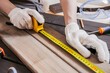 Carpenter is measuring length of wood planks or timbers by measuring tape or ruler. Carpenter workspace, craftsman entrepreneur.