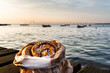 Bag of cinnamon rolls on a wooden boardwalk by the ocean at dusk with the Oresund Bridge in the background. Cosy Swedish fika break by the Baltic sea at sunset with typical Scandinavian pastry