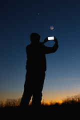 Wall Mural - silhouette of a man with smartphone and countryside under evening skies.
