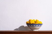 Yellow Lemons In A Ceramic Bowl On A Wooden Table Against A White Wall. Copy Space.