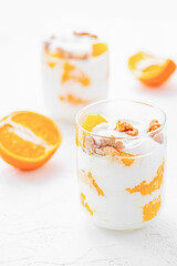 Wall Mural - Greek yogurt with orange and walnuts in glasses on a white table. Healthy food. Health eating concept. Selective focus.