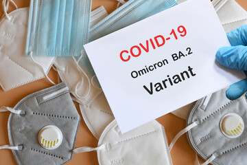 Doctor's hand in blue glove with white paper and text Covid-19 Omicron BA.2 Variant with various protection masks on background. COVID-19 Omicron BA.2 Variant strain protection concept.