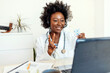© Jelena Stanojkovic - Young African-American female doctor giving online consultation to his patient office. A young doctor sitting in her office showing her patient the pills he needs. Healthcare concept.