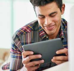 Poster - Checking his social media feeds. Shot of a handsome young man using his tablet while relaxing on the sofa at home.