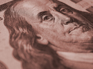 Wall Mural - American paper money background. A $100 bill with focus on Benjamin Franklin eye. US banknote close-up. Dark brown tinted wallpaper about economy and the USA dollar. Macro
