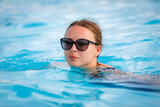 Fototapeta Przestrzenne - A young, beautiful girl in sunglasses swims in the pool. High quality photo