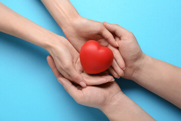 Wall Mural - People holding red decorative heart on light blue background, top view. Cardiology concept