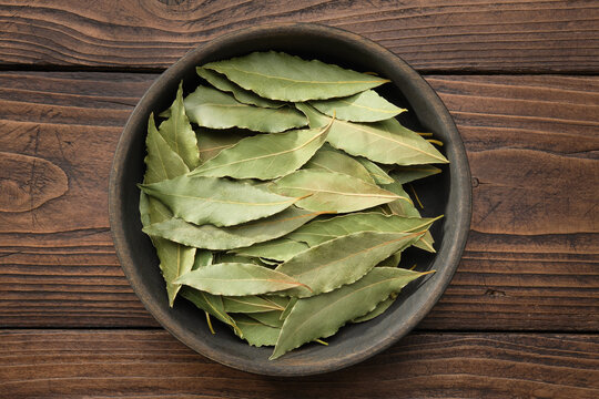 Wooden bowl of dried laurel leaves. Green bay leaves on wooden board, top view.