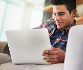 Poster - Spending a little time online. Shot of a handsome young man using his laptop while relaxing on the sofa at home.