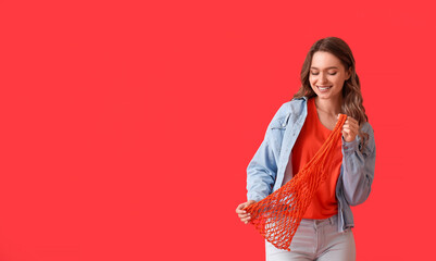 Wall Mural - Pretty young woman with string bag on red background