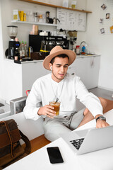 Poster - Young man with glass of cocktail using laptop at table in cafe