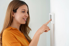 Portrait Of Beautiful Woman Lowering The Temperature For Energy Saving. Woman Adjusting Digital Central Heating Thermostat At Home.