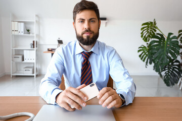 Canvas Print - Handsome young businessman with mobile phone at table in office