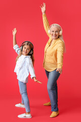 Wall Mural - Little girl and her grandma in headphones dancing on red background