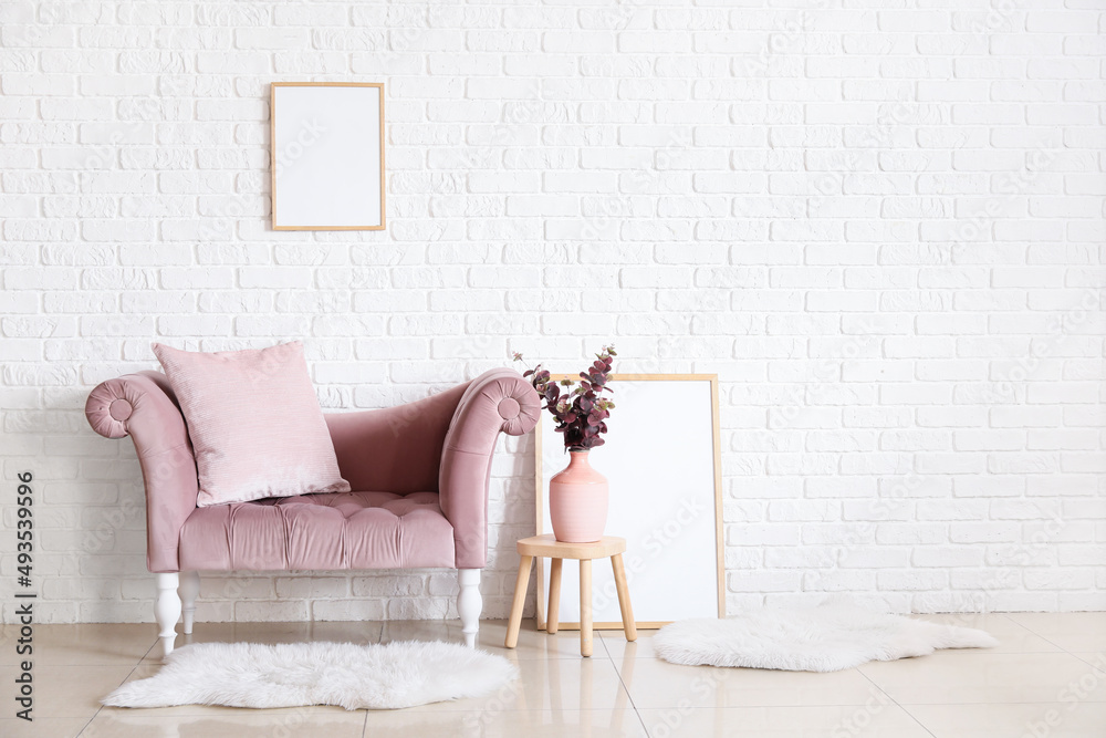 Stylish sofa and blank frames near white brick wall