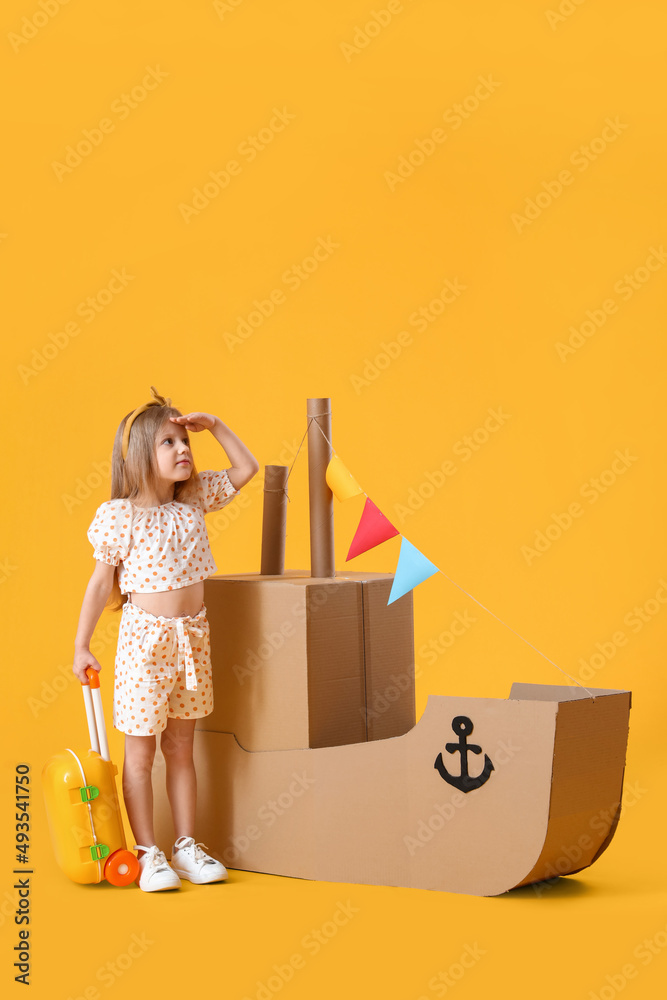Cute little girl playing with cardboard ship on yellow background