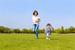 青空を背景に緑の芝の上で一緒に走る母と幼い女の子。親子,幸せ,愛情,育児のイメージ