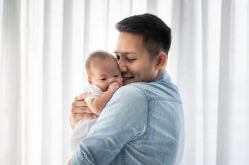 asian father holding baby daughter and kissing with love at home