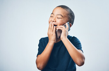 Poster - A call from grandma always gives him the giggles. Studio shot of a cute little boy looking amazed while using a smartphone against a grey background.