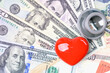 Cardiac care and heart health insurance, healthcare concept : Red heart and a stethoscope on US dollar notes, depicting compensation for the treatment costs and expenses caused from heart disease.