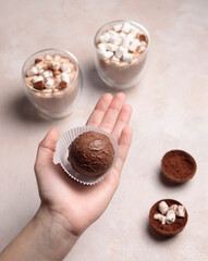 Chocolate bombs with cocoa and marshmallows for making a hot aromatic drink. The hand holds a chocolate ball. Glasses of cocoa in the background.