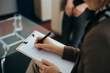 Close up of mental health professional takes notes during counseling with a patient.