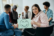 © Drazen - Young happy woman holds placard with drawn smiley face during group therapy meeting at mental health center.
