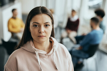 Wall Mural - Young woman stands in front of participants of group therapy at mental health center and looks at camera.