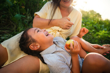 European mother and her Asian daughter in the apple garden in summer