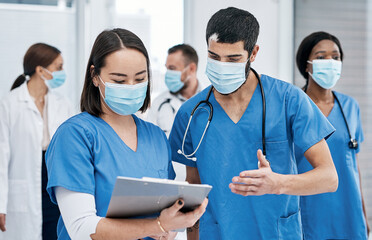 Poster - Discussing what to do next. Shot of two medical practitioners going through notes in a busy hospital.