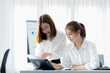 © kamiphotos - Atmosphere in the office of a startup company, two female employees are discussing, brainstorming ideas to working on summaries and marketing plans to increase sales and prepare reports to managers.
