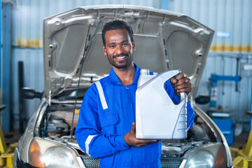 Car mechanic at garage with Oil container in hand looking at camera - concept of car maintenance, lubrication and repair service