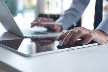 Poster - close up of businessman working on laptop computer and using digital tablet in office with blurred b