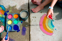 A Child Paints A Rainbow With Chalk Paint On A Cement Sidewalk