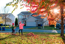 Two Children Rake Leaves In Front Of Their House
