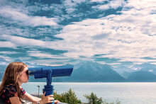 A Young Girl Looks Through Tourist Binoculars Toward A Fjord In Alaska