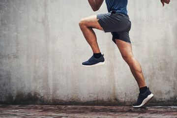 Wall Mural - Set off to the finishing line. Closeup shot of an unrecognizable man running against a grey wall outdoors.