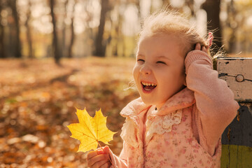 Cute little girl playing with leaves in the fall forest. Happy child girl laughing in the autumn park. Kid and autumn season concept.