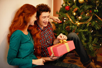 Canvas Print - Sharing Christmas with someone special. Shot of a young man opening his christmas present while sitting with his girlfriend.